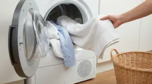 Una persona estrae asciugamani e una camicia dall’asciugatrice aperta, con cesto della biancheria accanto